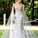 A bride in a long white wedding gown, standing gracefully and striking a pose in an outdoor grass area, surrounded by trees and plants