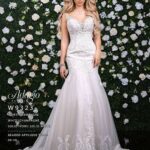 A girl in an ivory white long gown, posing in front of a wall full of white flowers and green plants