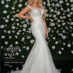 A girl in an ivory white long gown, posing in front of a wall full of white flowers and green plants