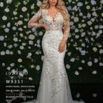 A girl in an ivory white long gown, posing in front of a wall full of white flowers and green plants