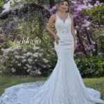 Bride in an ivory white long wedding gown, posing in front of green plants with purple flowers, on a grassy area