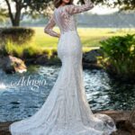 Bride in an ivory white long gown, posing with her back to the camera in front of a water pool surrounded by trees