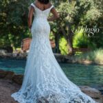 Bride in an ivory white long gown, posing with her back to the camera in front of a water pool surrounded by trees