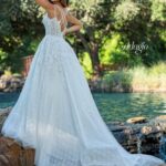 Bride in an ivory white long gown, posing with her back to the camera in front of a water pool surrounded by trees