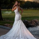 A bride in a long white wedding gown, turned back and striking a pose in an outdoor area, surrounded by trees and plants